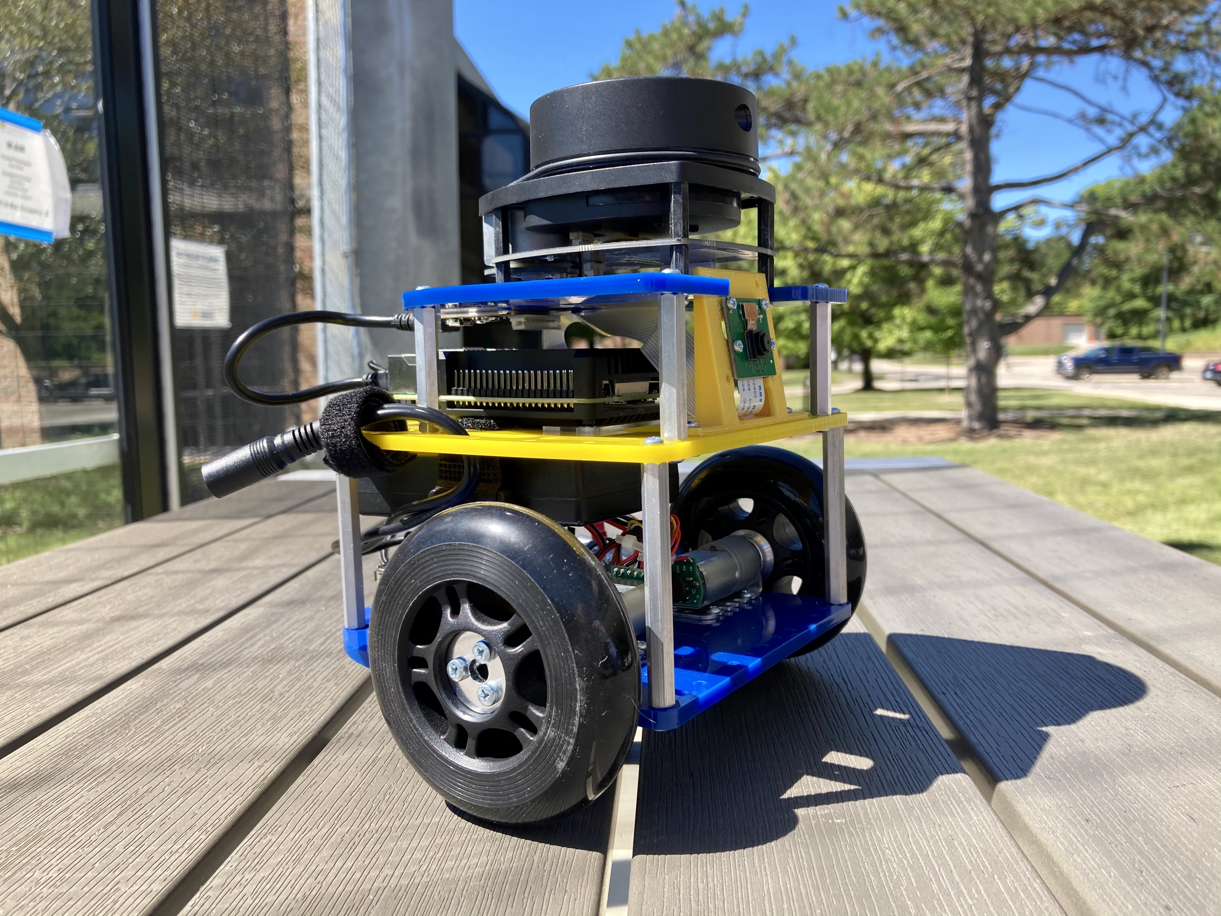 A wheeled MBot with a LiDAR scanner and other onboard electronics on an outdoor table.